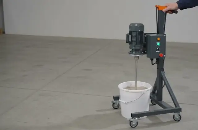 Blunger mixing clay slip in a bucket, operator's hand on the handle — frame from factory footage; batch size is not in frame